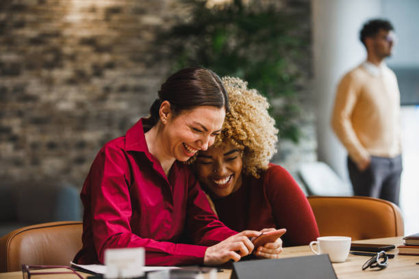 Two female colleagues bonding while looking at funny memes during coffee break stock photo