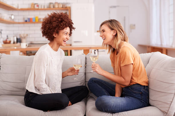 Two Female Friends Relaxing On Sofa At Home With Glass Of Wine Talking Together Two Female Friends Relaxing On Sofa At Home With Glass Of Wine Talking Together female friendship stock pictures, royalty-free photos & images