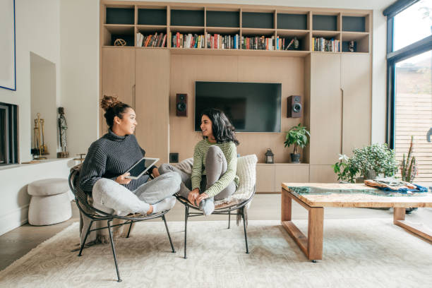Two female friends sitting in a living room Two female friends sitting in a living room roommate stock pictures, royalty-free photos & images