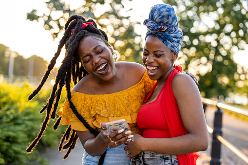 Two female friends with smartphone, smiling outdoors