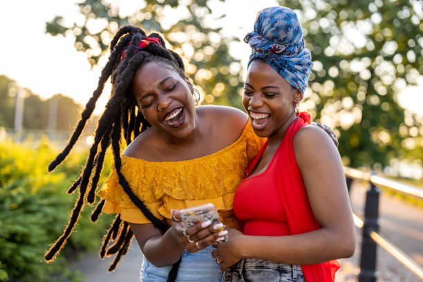 Two female friends with smartphone, smiling outdoors Two female friends with smartphone, smiling outdoors braided hair photos stock pictures, royalty-free photos & images