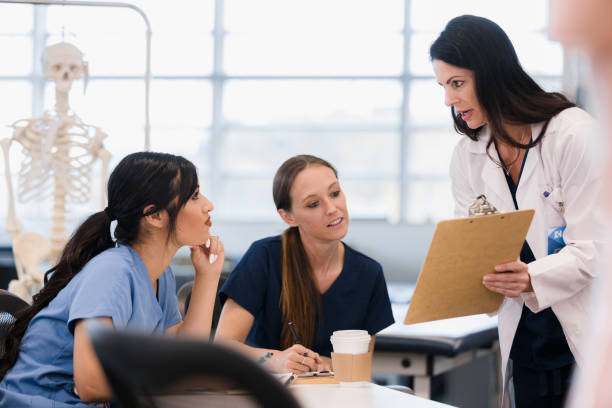 Two female nursing students look at information teacher shows them Two female nursing students listen as the mid adult female professor gives them some information. best medical schools stock pictures, royalty-free photos & images