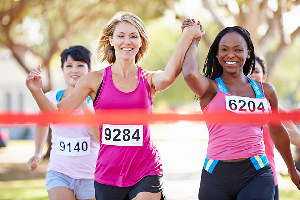Two Female Runners Finishing Race Together Two Female Runners Finishing Race Together Holding Hands In The Air Smiling marathon photos stock pictures, royalty-free photos & images