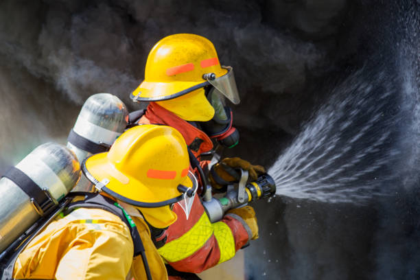 two firefighters water spray by high pressure nozzle to fire surround with smoke and copy space stock photo