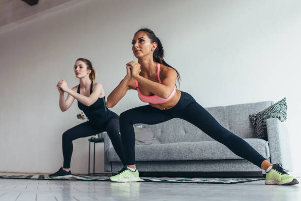 Two fit girls doing home workout performing lateral lunges at home Two fit girls doing home workout performing lateral lunges at home. lateral surface photos stock pictures, royalty-free photos & images