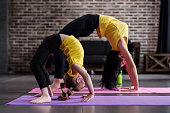 Two flexible girls of different age doing upward facing bow yoga pose working out.