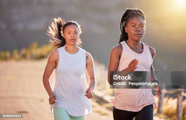 Two focused young female athletes out for a run on a mountain road on a sunny day. Energetic young women running outdoors to help their bodies in shape and fit. Two sportswomen exercising together