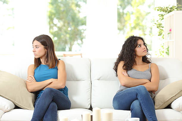 Two friends angry after quarrel Two angry friends after a quarrel sitting on a couch and looking at the other side arguing stock pictures, royalty-free photos & images