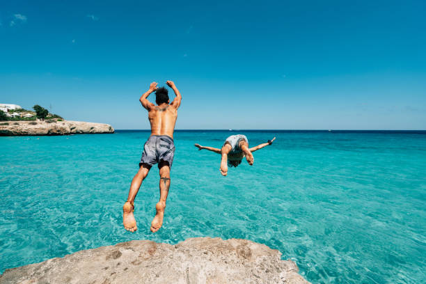Two friends are diving in the sea from a cliff stock photo