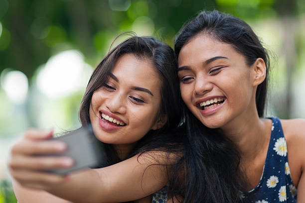 Two friends having fun taking a selfie Two young women outdoors in a park taking a selfie with a smartphone. philippine girl stock pictures, royalty-free photos & images