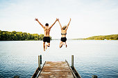 Zwei Freunde, die gemeinsam vom Steg am See springen