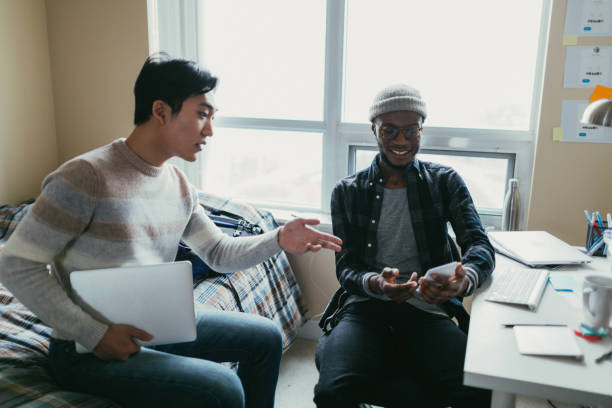 Two friends talking in a dorm room African american and asian men chatting in a dormitory room. college dorm stock pictures, royalty-free photos & images