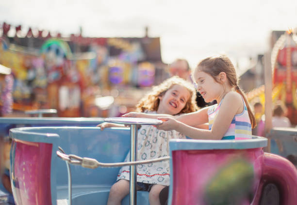 Two girls at a fairground Two happy little girls are spinning around on a tea cup ride at an amusement park amusement park ride stock pictures, royalty-free photos & images