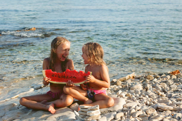 Two girls eating watermelon on the beach stock photo