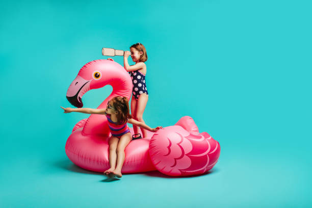 Two girls playing on inflatable toy Two girls on inflatable toy flamingo with binoculars. Small friends in swimsuits playing on inflatable mattress over blue background. little girls in bathing suits stock pictures, royalty-free photos & images