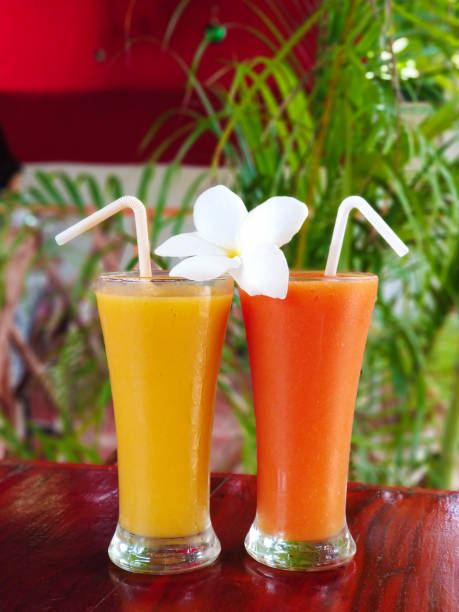 Two glass glasses with freshly squeezed juice and frangipani flower Two glass glasses with freshly squeezed juice and frangipani flower. papaya smoothie stock pictures, royalty-free photos & images