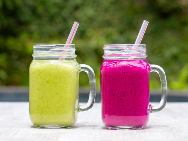 Two glass mugs with fresh smoothies from a dragon fruit, banana, mango, avocado, broccoli and honey. Island Bali, Ubud, Indonesia Two glass mugs with fresh smoothies from a dragon fruit, banana, mango, avocado, broccoli and honey. Island Bali, Ubud, Indonesia. Close up papaya smoothie stock pictures, royalty-free photos & images