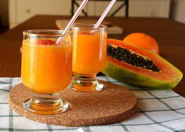 Two glasses of fresh orange and papaya smoothie. Two glasses of fresh orange and papaya smoothie on a wooden table.  papaya smoothie stock pictures, royalty-free photos & images