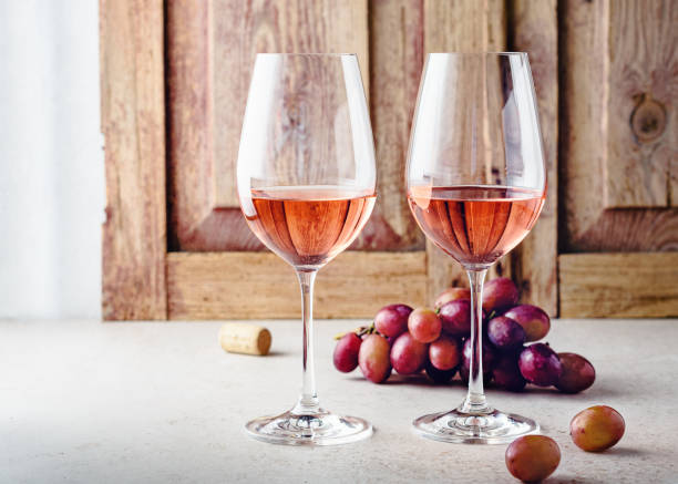 Two glasses of rose wine. Two glasses of rose wine and a bunch of grapes on a light wooden background. rose colored stock pictures, royalty-free photos & images