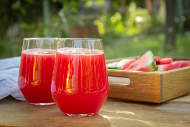 Two glasses with fresh watermelon juice on a table in the garden. Wooden tray with watermelon slises Two glasses with fresh watermelon juice on a table in the garden. Wooden tray with watermelon slises watermelon juice stock pictures, royalty-free photos & images