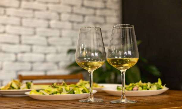 Two glasses with white wine and green salad with cucumber and radish daikon. An appetizer for a banquet or buffet. Grey tiled wall. stock photo