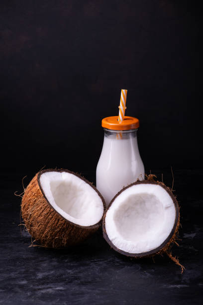 Two halves of a coconut, and coconut milk in the bottle front view, two halves coconut and coconut milk in the glass bottle, on dark background coconut milk stock pictures, royalty-free photos & images