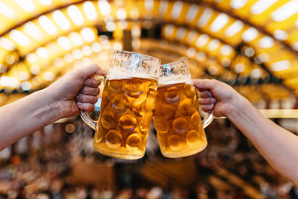 two hands clinking beer glasses in octoberfest marquee - duits bier stockfoto's en -beelden