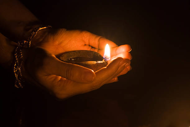 Two hands holding a small lit oil lamp in the dark stock photo