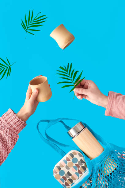Two hands with bamboo cup and palm leaf. Zero waste tea in in eco friendly insulated bamboo flask. Net.bag with lunch box and tea flask. Surreal levitation on vibrant blue mint background. Surreal levitation on vibrant blue mint background. Two hands with bamboo cup and palm leaf. Zero waste tea in in eco friendly insulated bamboo flask. Net.bag with lunch box and tea flask. bamboo material stock pictures, royalty-free photos & images