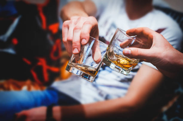 Two hands with whiskey Two hands clink glasses of whiskey at home,on the couch, cozy drinking stock pictures, royalty-free photos & images