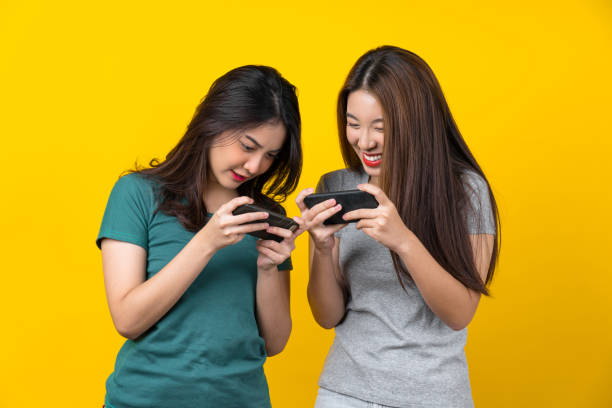 Two Happiness Asian smiling young woman gamer using smart mobile phone and playing games on isolated yellow color background Two Happiness Asian smiling young woman gamer using smart mobile phone and playing games on isolated yellow color background, Lifestyle and leisure with hobby concept cute thai girl stock pictures, royalty-free photos & images
