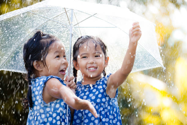 Two happy asian little girls with umbrella having fun to play with the rain together Two happy asian little girls with umbrella having fun to play with the rain together in vintage color tone cute thai girl stock pictures, royalty-free photos & images
