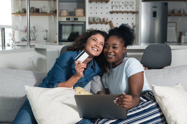 Two happy carefree young women business partners and owners, friends sitting on the sofa are happy because they have just tried online shopping with credit cards on their new internet store website. stock photo
