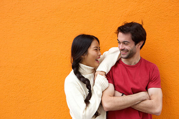Two happy friends laughing against orange background stock photo