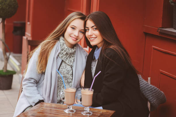 two happy girl friends talking and drinking coffee in autumn city in cafe. Meeting of good friends, young fashionable students with natural make up. stock photo