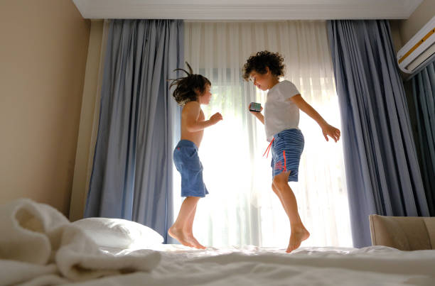 Two happy kids jumping on the bed with a phone listening to music stock photo