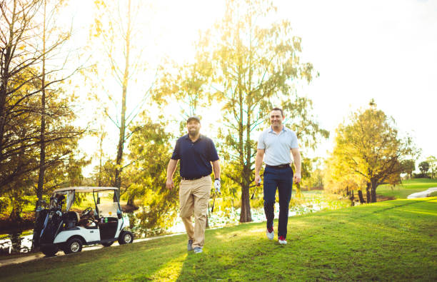 Two happy relaxed male golfers with golf clubs walking on a golf course together stock photo