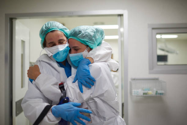 twee gezondheidswerkers omhelzen in viering van een succesvolle chirurgieprocedure - arts vrouw mondkapje stockfoto's en -beelden