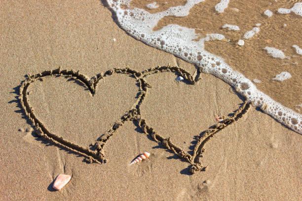 Two hearts in the sand on the beach. Waves with foam blue  sea on a sunny sandy beach in resort on summer vacation rest. Two hearts in the sand on the beach. Waves with foam blue  sea on a sunny sandy beach in resort on summer vacation rest. divorce beach stock pictures, royalty-free photos & images