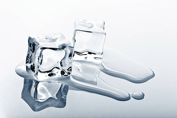 Two ice cubes melting on reflected surface stock photo