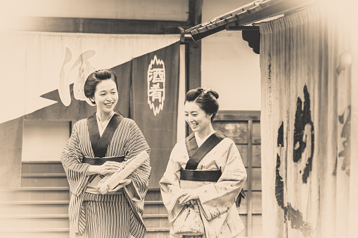 Vintage styled image composition of Japanese women dressed traditionally in Kimono and talking a stroll around their village.