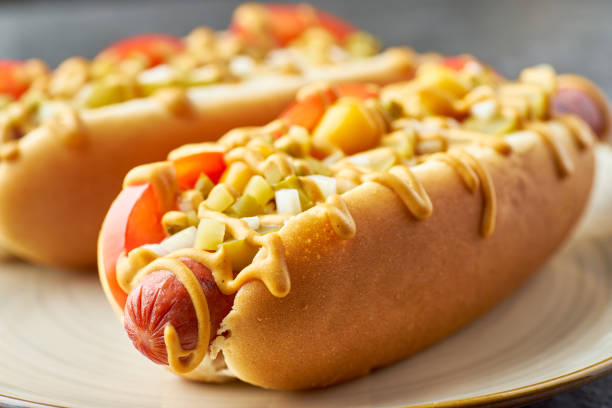 Two juicy hot dogs close-up on dish over stone table Two juicy hot dogs close-up on dish over stone table. Selective focus hot dog stock pictures, royalty-free photos & images