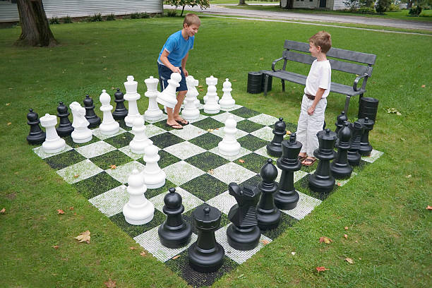 Two kids playing a chess game with large pieces on grass Young boys playing lawn chess. gchutka stock pictures, royalty-free photos & images