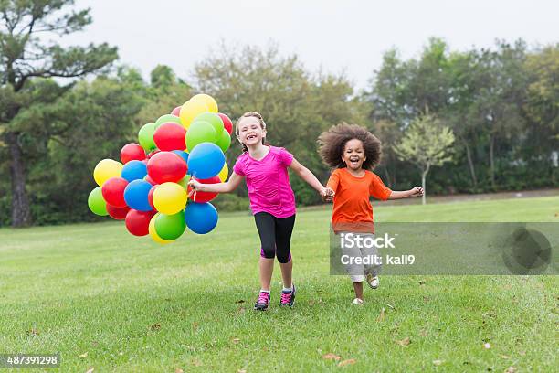 Two little girls running with bunch of balloons at park