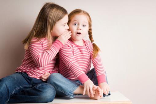 Color photo of a five-year-old girl whispering secrets to her three-year-old sister.