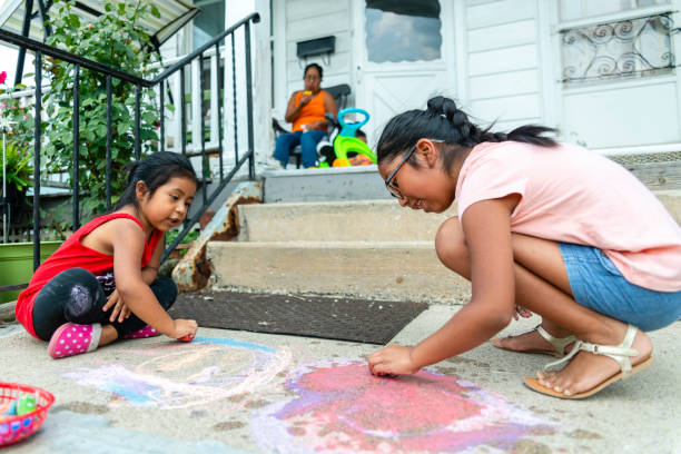 Two little Latino Mexican-American girls, sisters, drawing with chalk at the porch of his house in Pennsylvania Two little Latino Mexican-American girls, sisters, drawing with chalk at the porch of his house in Pennsylvania, USA at the sunny summer day hot mexican girls stock pictures, royalty-free photos & images