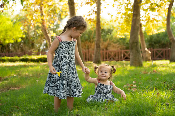 twee llittle zusters wandelen en plaatsings op het gras genieten van de zonnige dag - kunstof stockfoto's en -beelden