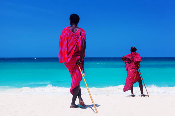 Two maasai warriors looking on ocean. Two maasai warriors looking at ocean on white sand beach at summer. maasai warrior stock pictures, royalty-free photos & images