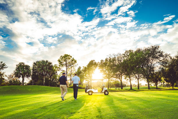 Two male golfers on a scenic golf course walk toward golf cart with sunflare stock photo
