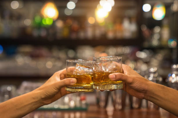 Two men clinking glasses of whiskey drink alcohol beverage together at counter in the pub. stock photo